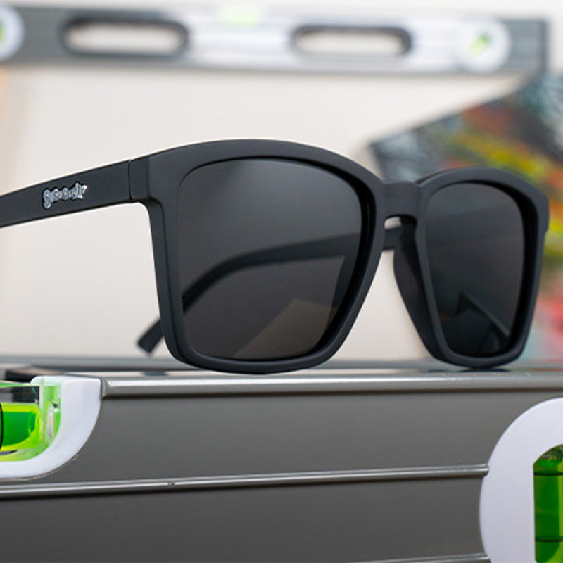 Three-quarter angle view of slim-fit black sunglasses with non-reflective black lenses sitting atop a spirit level.