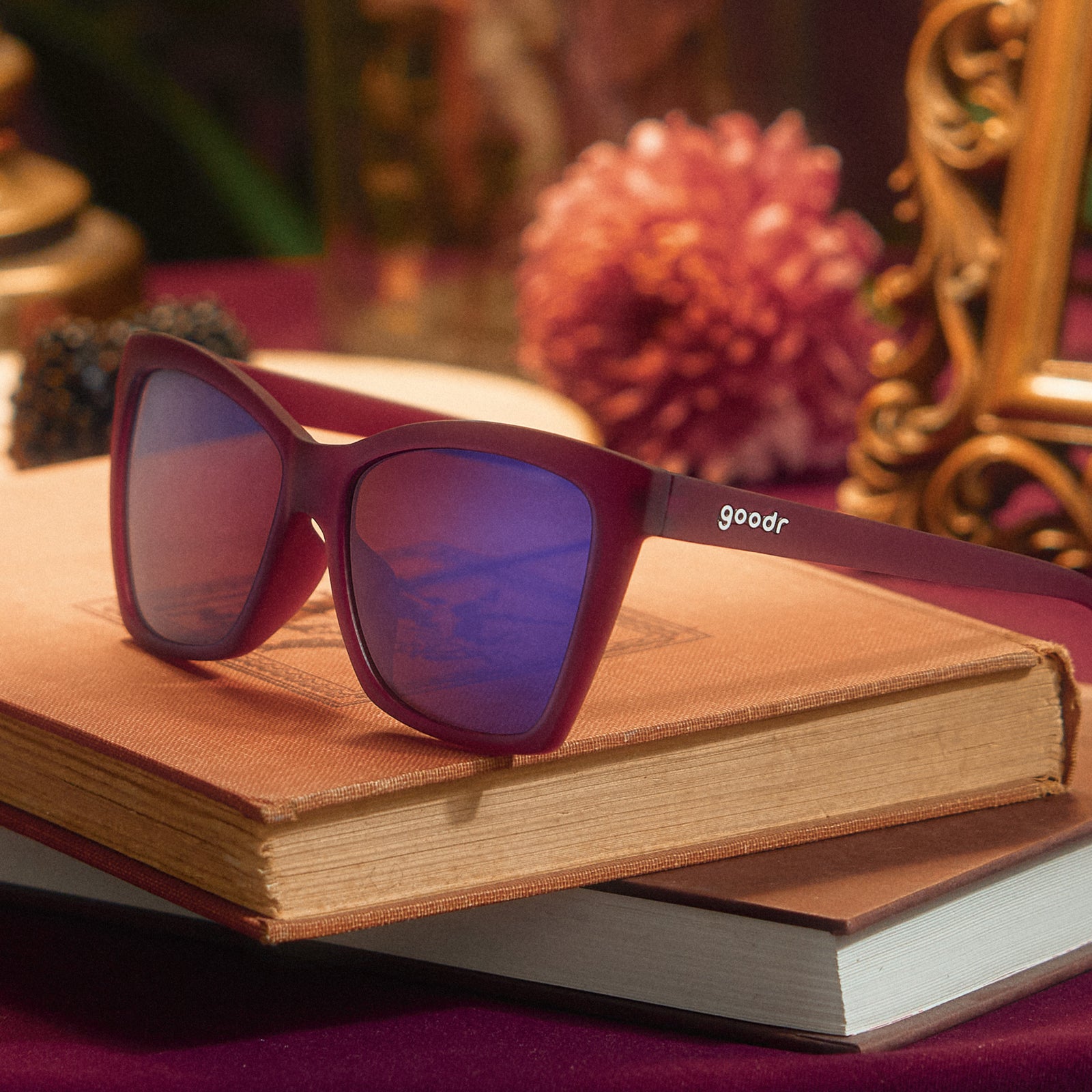 A pair of red violet Pop Gs rests on top of some vintage books, a gilded picture frame and pink dahlia are in the background.