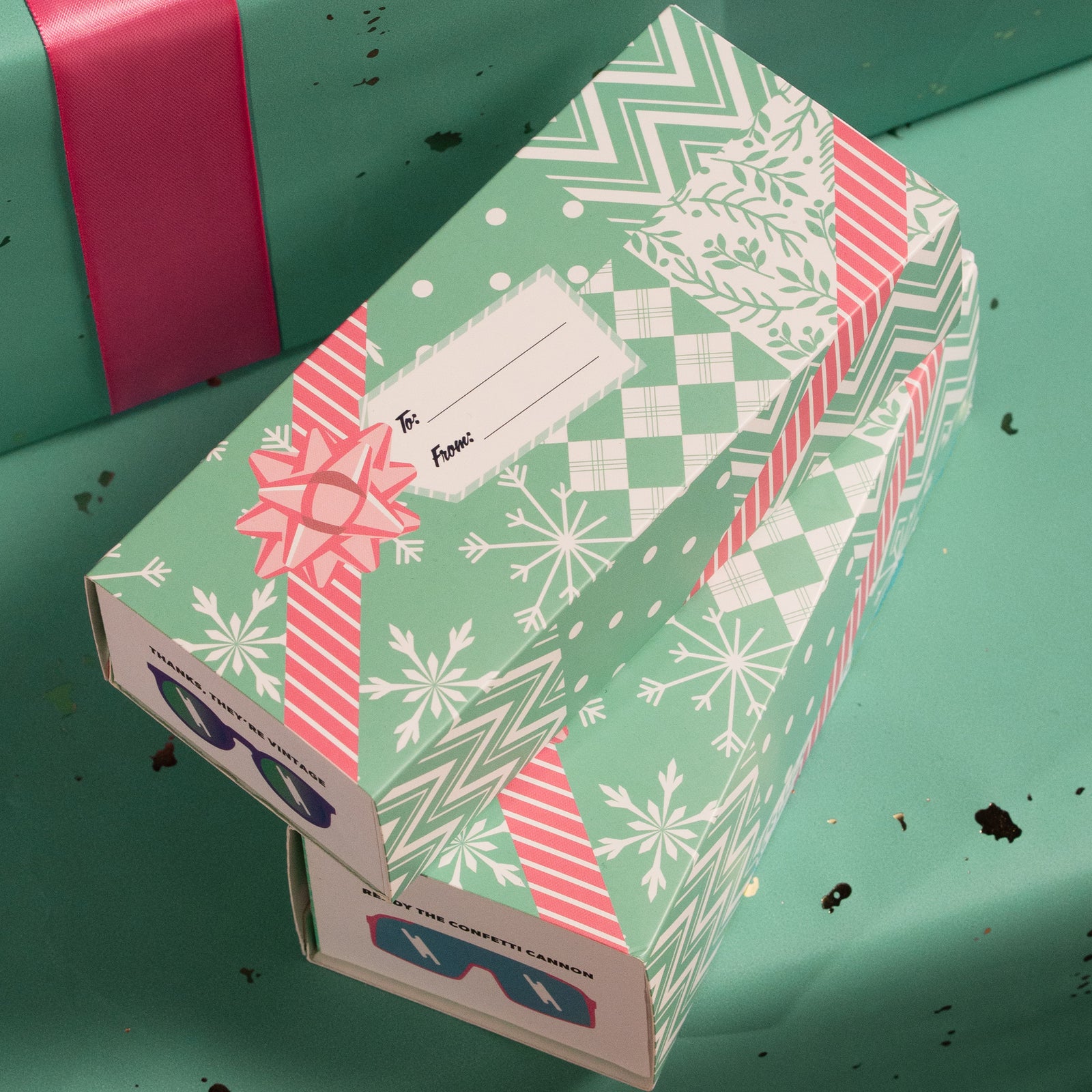 Sunglasses boxes wrapped in custom teal and pink festive sleeves, featuring 'To' and 'From' tags.