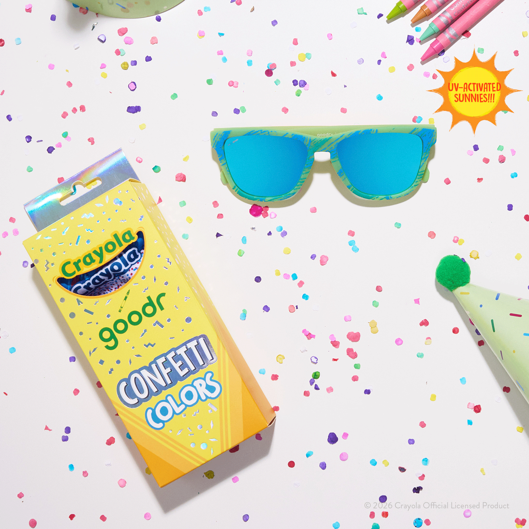 Crayola goodr Confetti Colors sunglasses with Crayola box packaging surrounded by colorful confetti and party supplies.