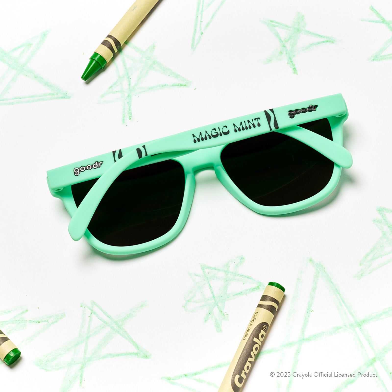 Back view of Magic Mint-colored Crayola sunglasses with green lenses on a white sheet with scribbled stars