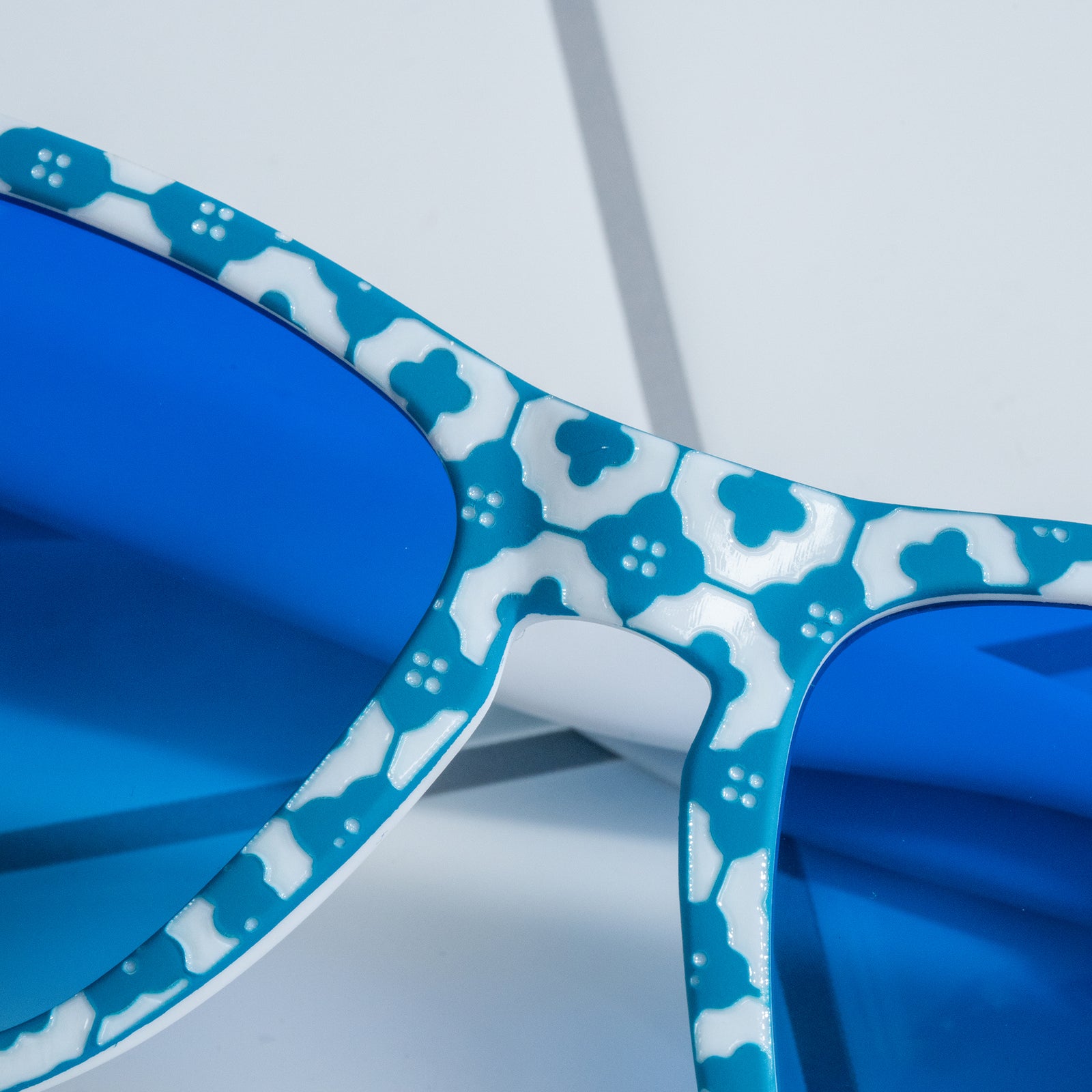 Close-up of the faceplate of blue-and-white tile-print shades with blue gradient lenses sitting on a white tiled surface.