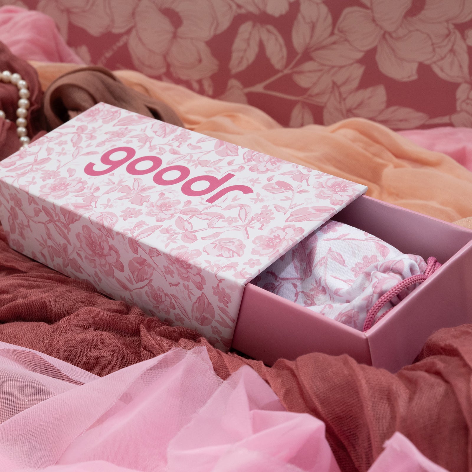 Custom packaging featuring a pink floral toile box and sunglasses pouch on top of different pink-colored fabric.
