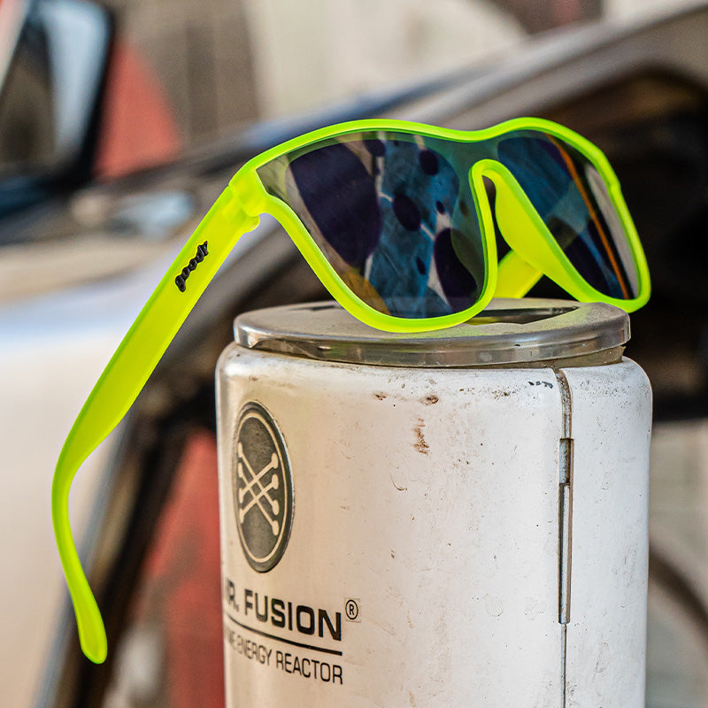 Square neon green sunglasses with a single mirrored chrome lens sitting atop a dangerous energy reactor.