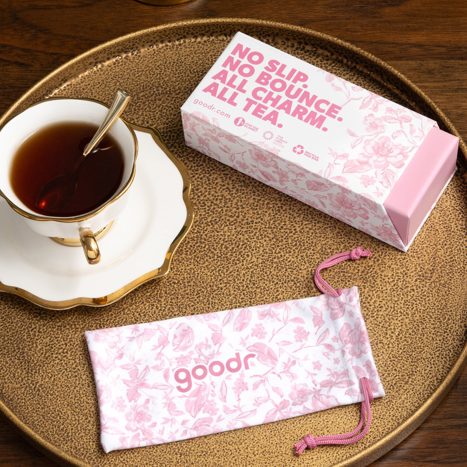Pink floral toile custom box and sunglasses pouch on a copper tray next to a tea-filled teacup.
