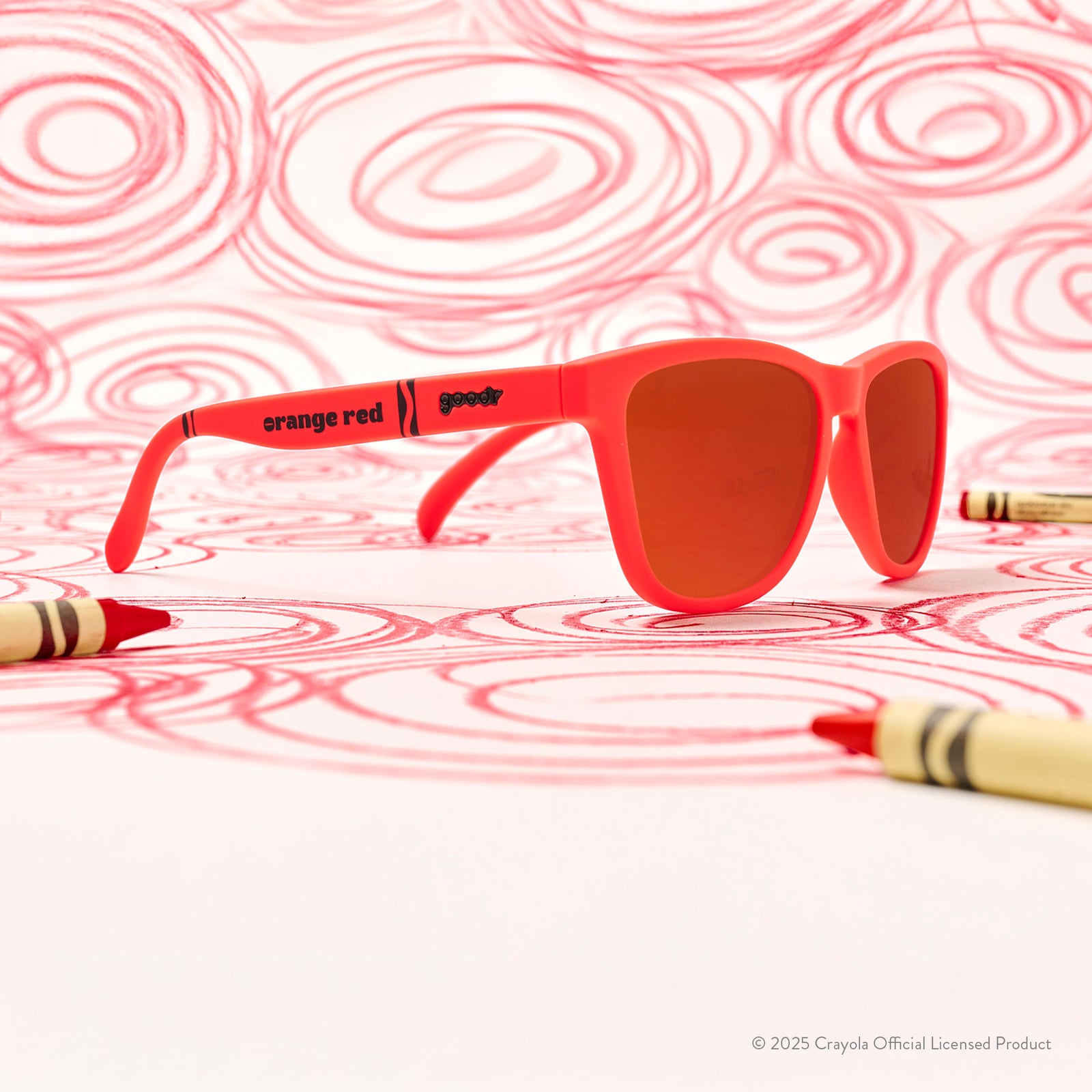 Three-quarter angle view of Orange Red  Crayola sunglasses on a white background with crayons and spiraling scribbles
