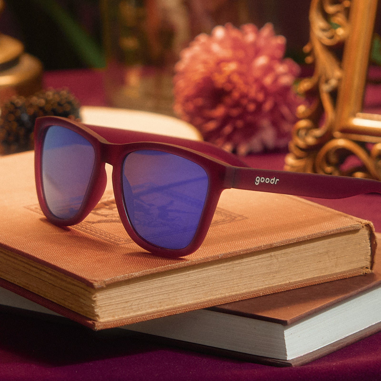 Three-quarter angle view of translucent purple sunglasses with reflective purple lenses on top of stacked books.