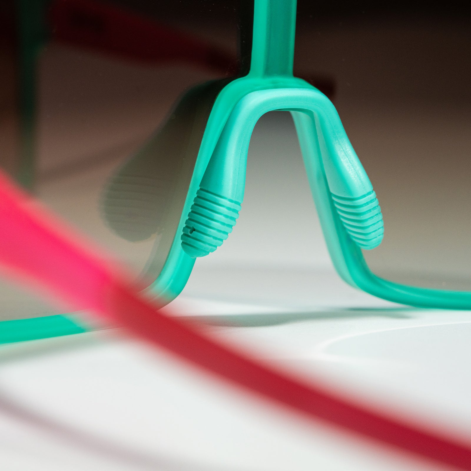 Close-up shot of a pair of teal and pink wrap sunglasses showing an adjustable nosepiece, photographed from behind.