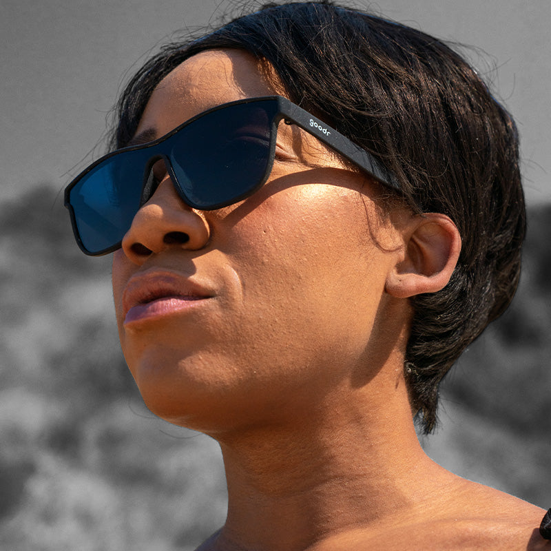 Three-quarter angle view of a woman wearing futuristic black flat single-lens sunglasses, looking off to the side.