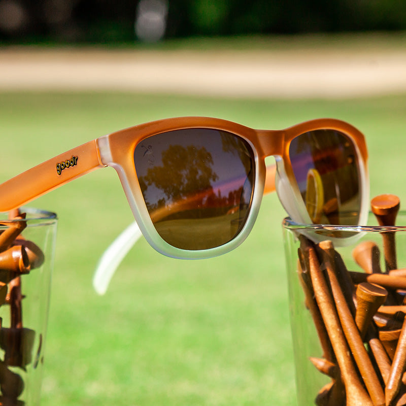 Three-quarter angle view of brown-to-white gradient sunglasses sitting atop drinking glasses field with brown golf tees.
