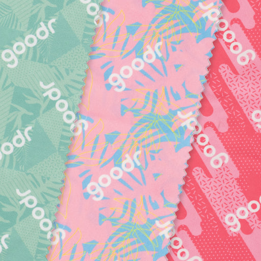 Close-up of three microfiber lens cloths with a geometric tropical print in shades of pink and teal overlapping each other.