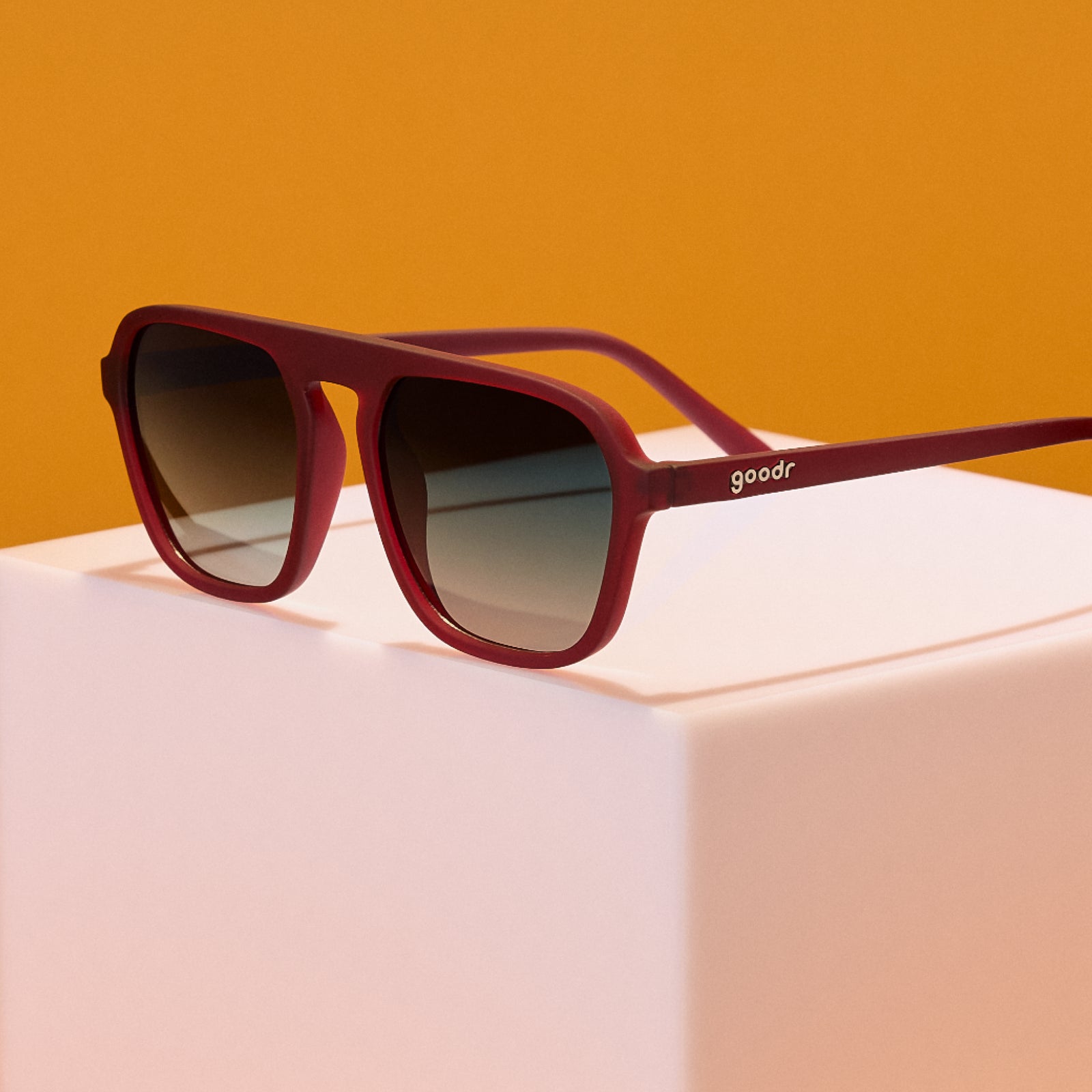 Red sunglasses with gradient lenses on a pink and orange gradient background