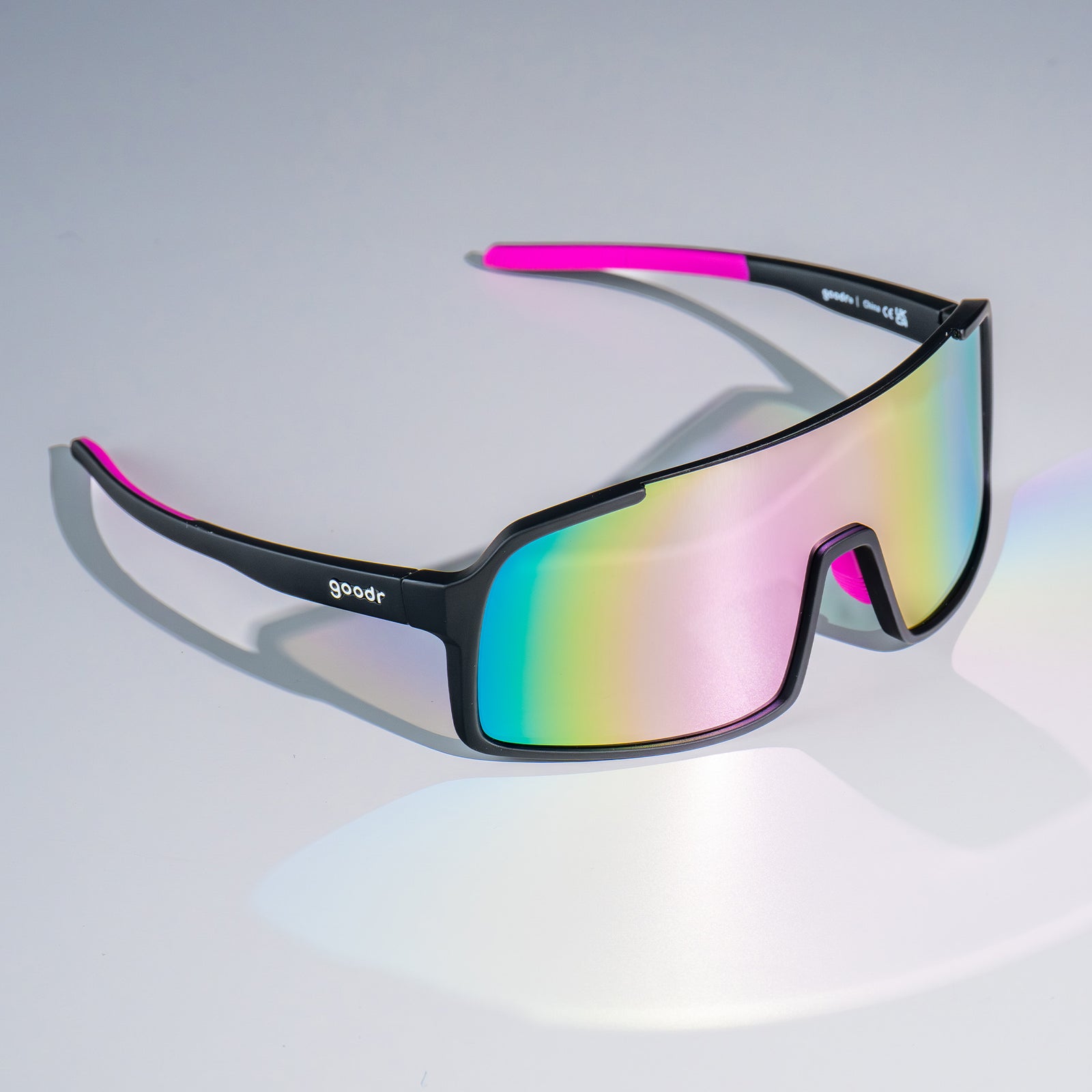 Three-quarter view of black wrap sunglasses with purple reflective lenses sitting on a white surface.