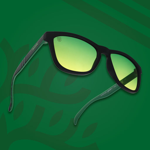 Three-quarter angle view of Austin FC shades tilted up. Green and black frames. Green-yellow lenses. Green background.