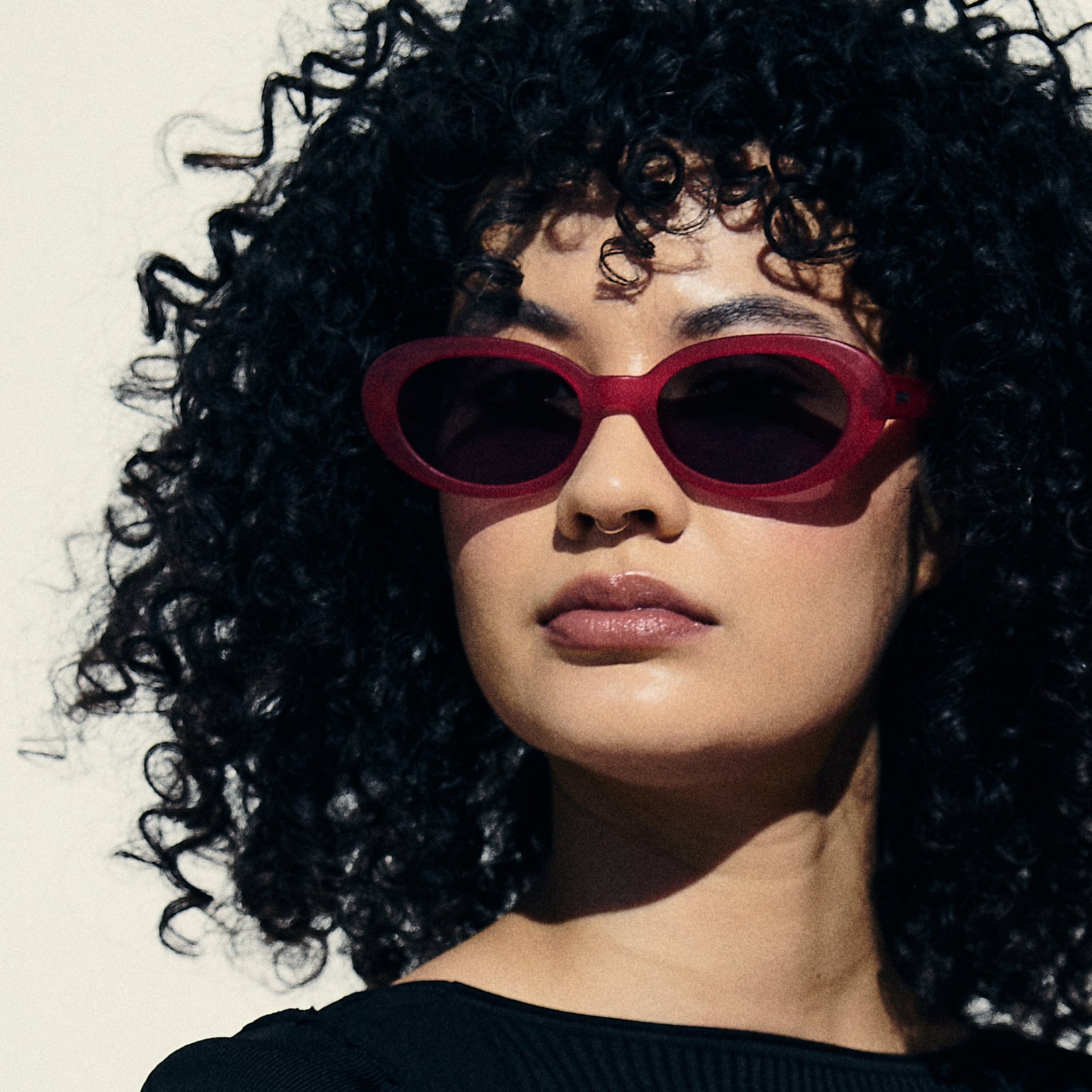 Portrait view of a woman wearing hot pink oval sunglasses with dark red polarized lenses.