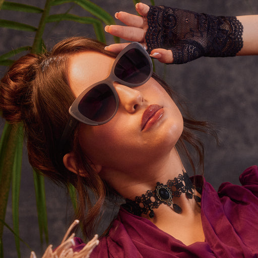 An elegantly dressed woman poses in translucent gray cat-eye sunglasses with black gradient lenses.