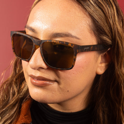 A sleek, stylish woman smirks to the side wearing brown tortoiseshell Grand Gs with brown non-reflective lenses.