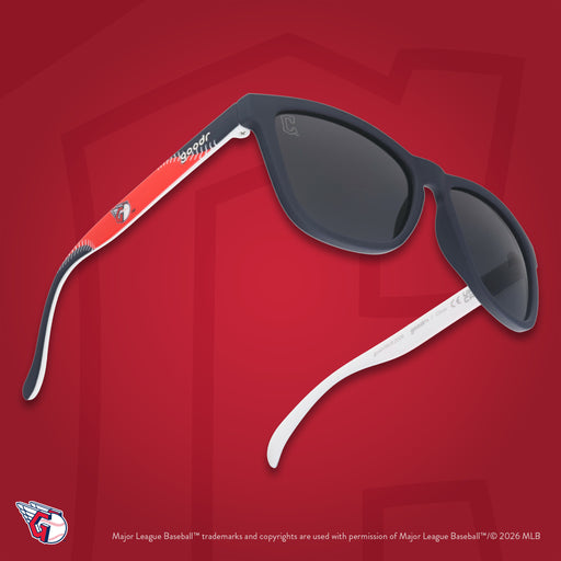 Three-quarter angle view of a pair of navy, red, and white Guardians sunnies floating against a red background featuring the C.