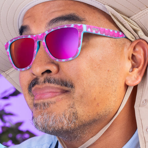 An optimistic-looking man wearing a floppy khaki hat rocks a pair of fuzzy, textured turquoise-and-wine shades with rose-reflective lenses.
