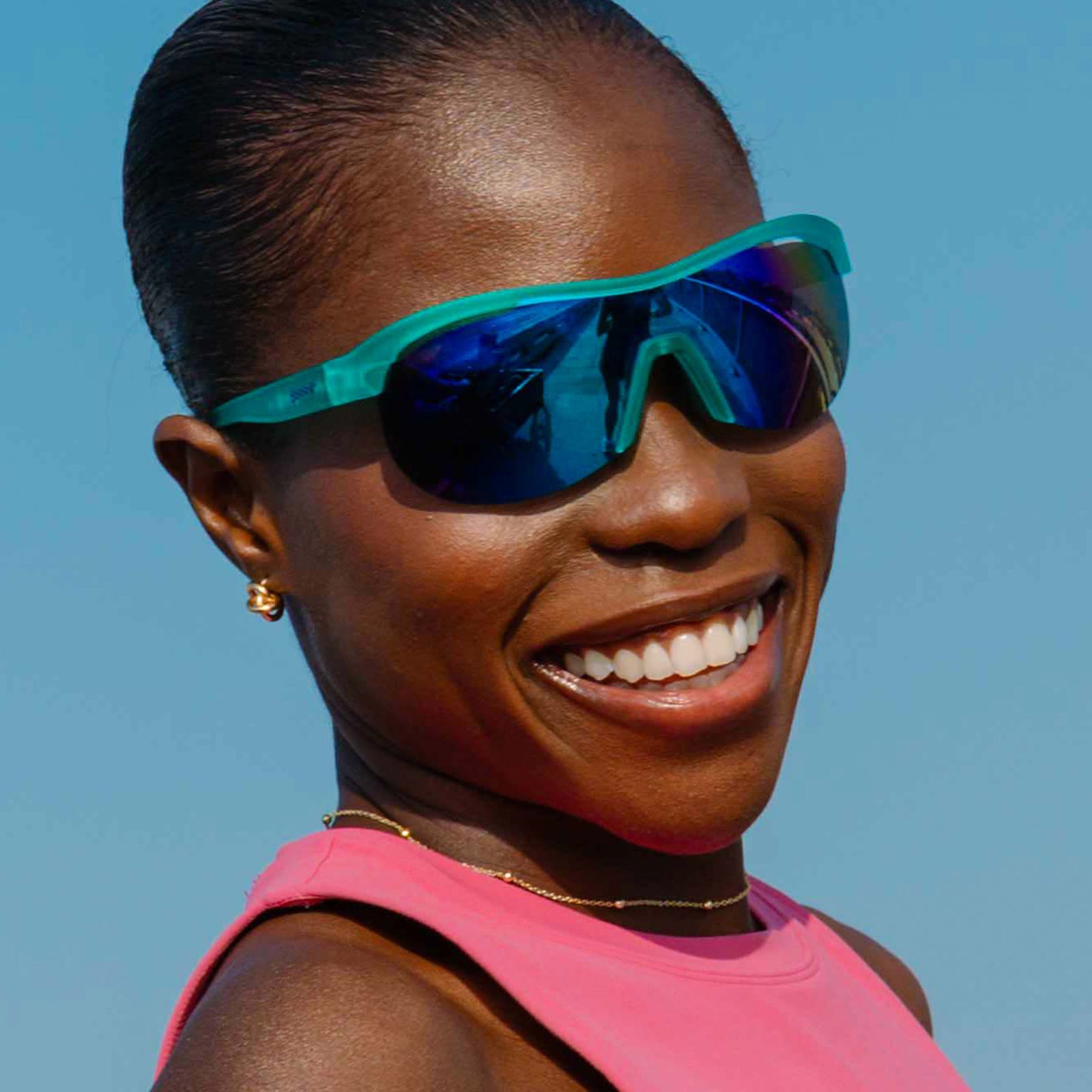 Low-angle view of a woman with a sleek bun wearing translucent mint green wrap shield sunglasses with white-blue reflective lenses.