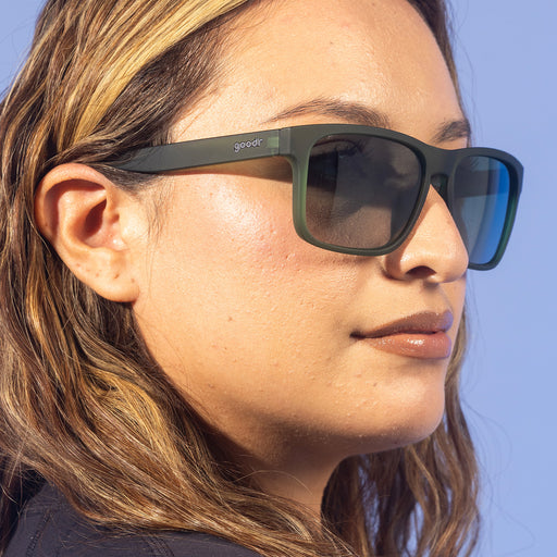 A fashionable woman with wavy blonde hair looks off in translucent dark green Grand Gs with green gradient lenses.