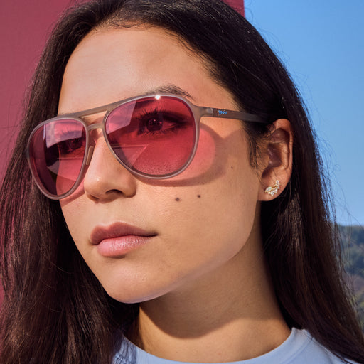 Woman wearing gray aviator sunglasses featuring pink gradient non-reflective lenses.