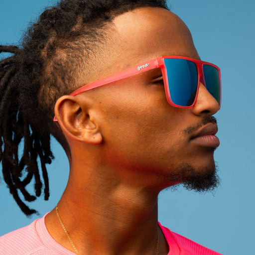 A closeup of a serious man, looking up in oversized pink flat-top glasses with blue reflective lenses.