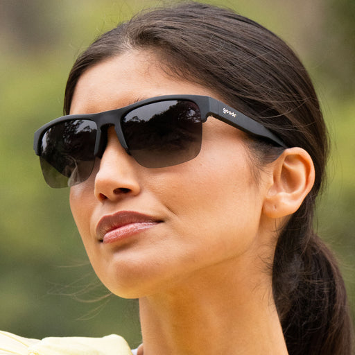 Close-up shot of woman outdoors wearing black half-rim sunglasses with all polarized black gradient lenses as she looks past the camera.