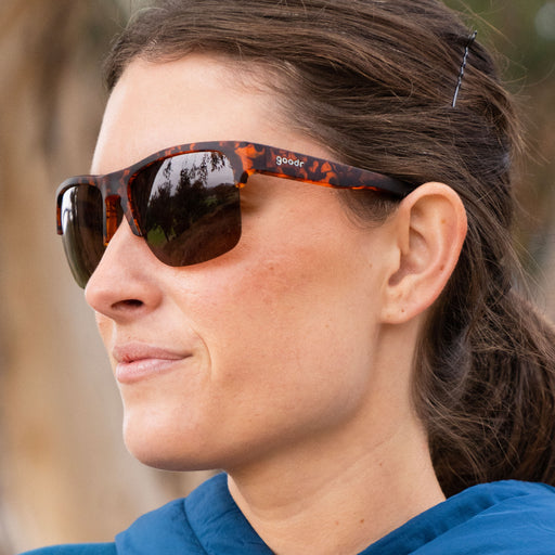 Close-up of a woman’s side profile as she smiles while wearing half-rim brown tortoiseshell sunglasses with brown non-reflective lenses.