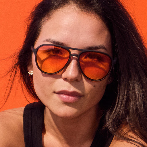 Woman wearing black aviator frames featuring orange-yellow gradient non-reflective lenses.