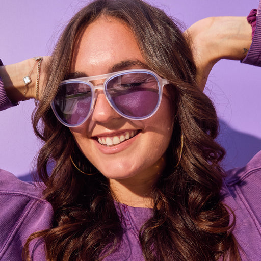 Smiling woman wearing clear aviator sunglasses featuring purple-blue gradient non-reflective lenses.