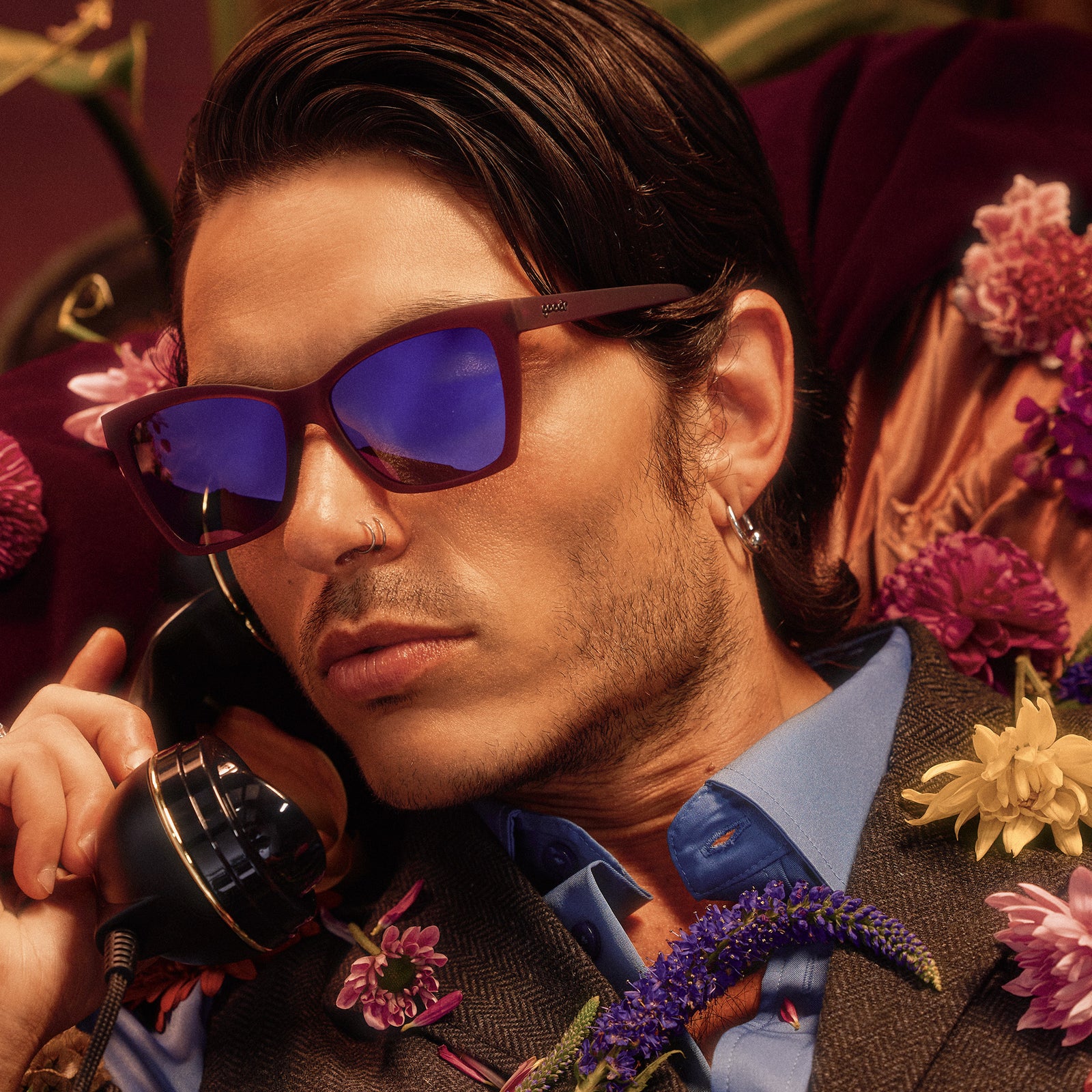 A handsome young man wearing red violet Pop Gs with purple lenses poses with a vintage phone, flowers scattered on his chest.
