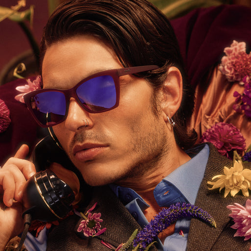 A handsome young man wearing red violet Pop Gs with purple lenses poses with a vintage phone, flowers scattered on his chest.