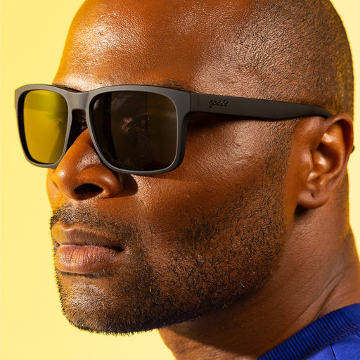 A fashionable man with dark, cropped hair looks off to the side, with black Grand Gs with black non-reflective lenses.