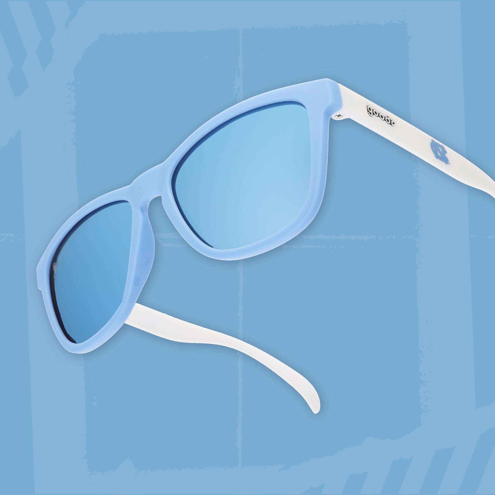 Three-quarter angle view of Carolina blue and white sunglasses featuring ice blue reflective lenses and the UNC logo on a light blue background.