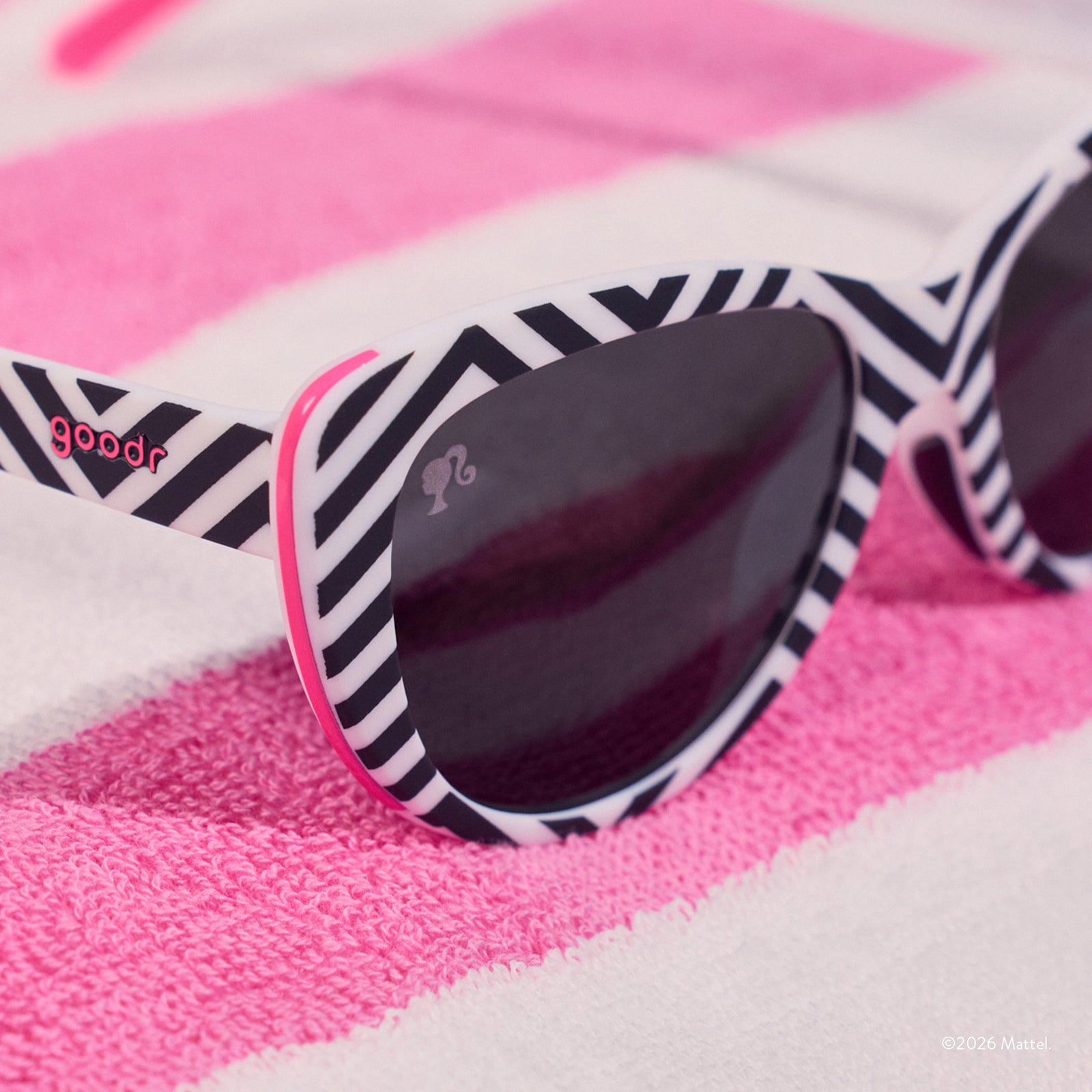 Close-up on the temple of black-and-white cat-eye sunnies with hot pink accents sitting on a pink and white beach towel.