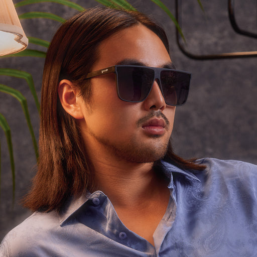 A young man with dark, shoulder-length hair poses in a pair of translucent gray Fly Gs against a dark gray background.