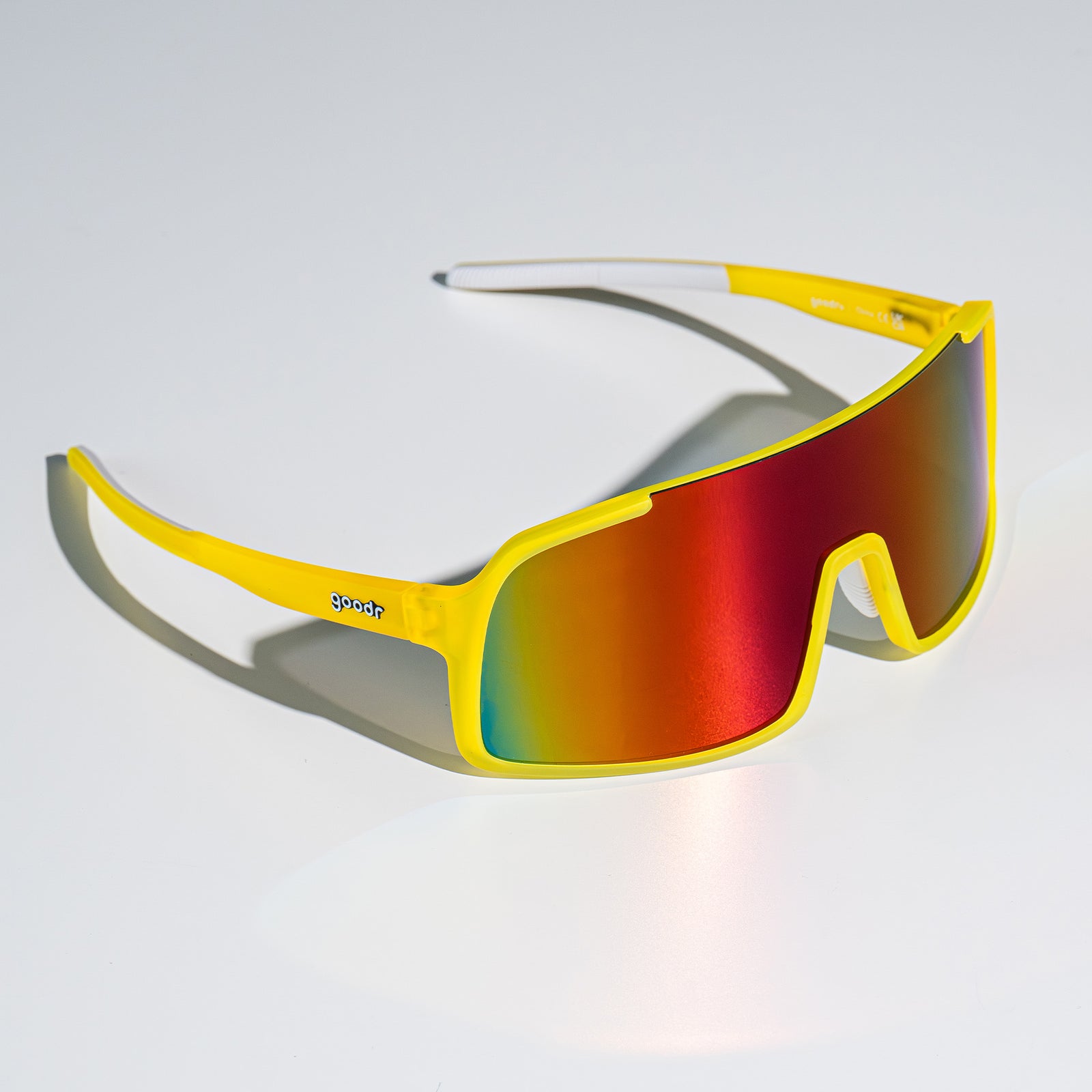 Three-quarter view of yellow wrap sunglasses with red reflective lenses sitting on a white surface.