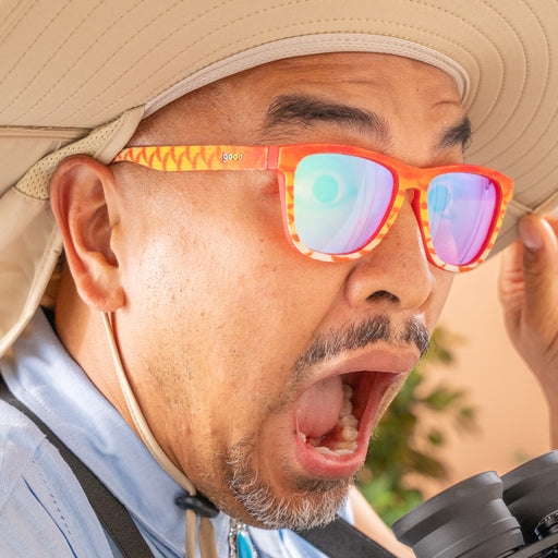 Close-up of a man in a wide-brim sun hat wearing red and yellow fuzzy sunglasses surprised by something off-camera.