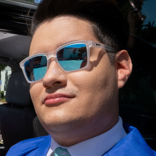 A suave-looking man in clear sunglasses with reflective blue lenses looks ahead confidently.