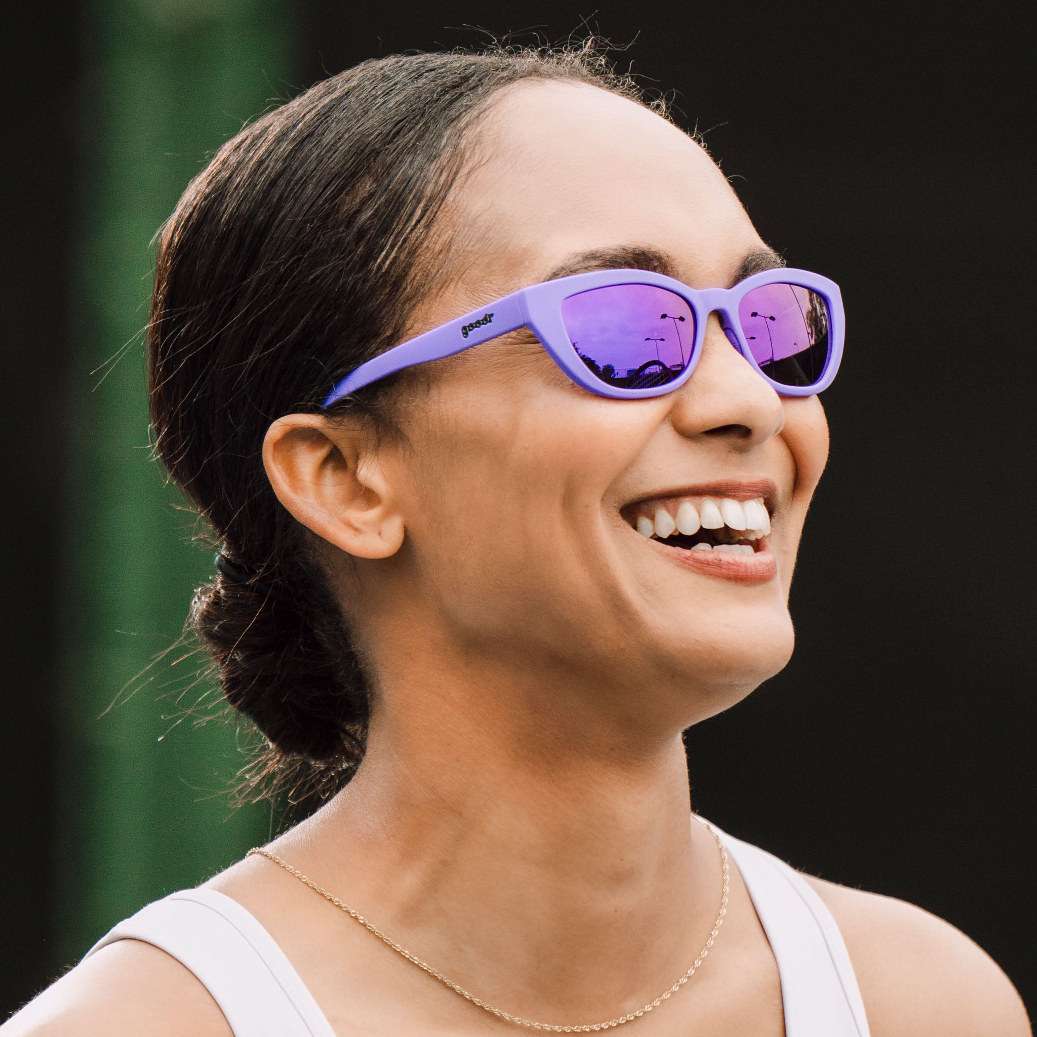 A woman with her dark hair pulled back smiles joyously in a pair of deep purple cat-eye Cheetah G sunglasses.