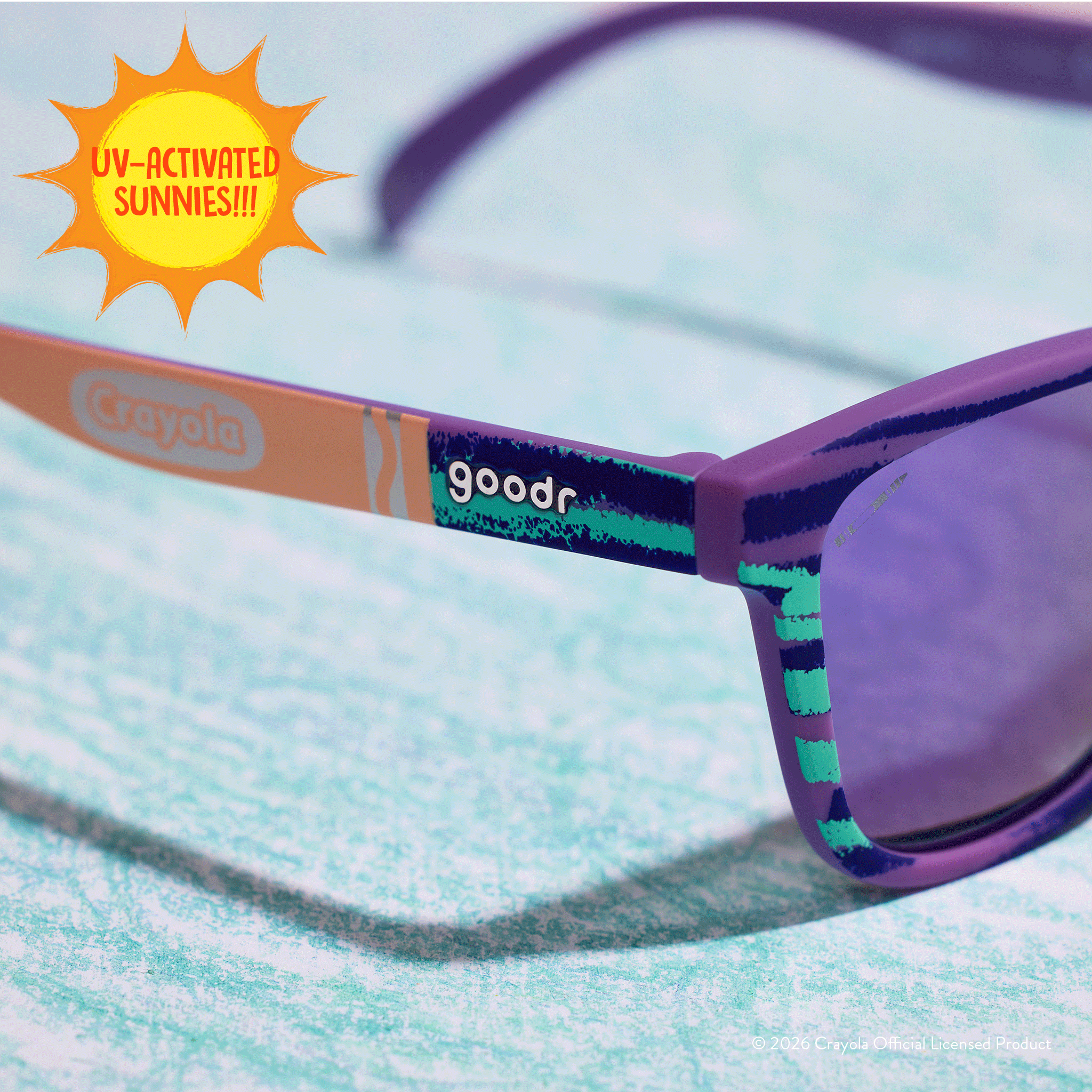 Close-up of Crayola goodr UV-activated sunglasses with green and purple frames and purple reflective lenses.