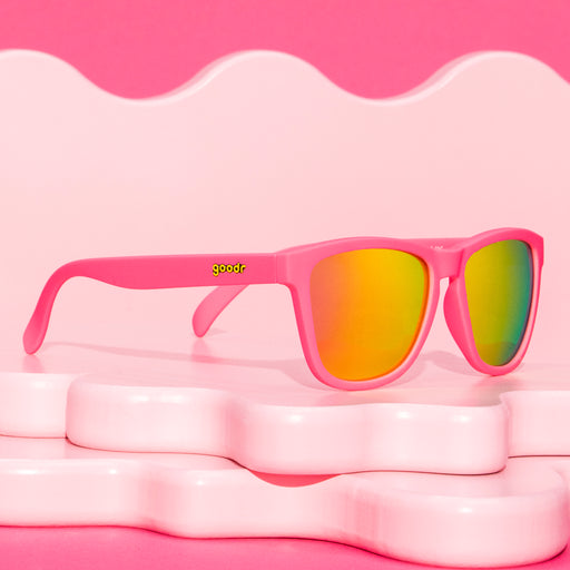 Three-quarter angle view of bright pink sunglasses with pink reflective polarized lenses resting on a warm pink wavy display representing antacid relief.