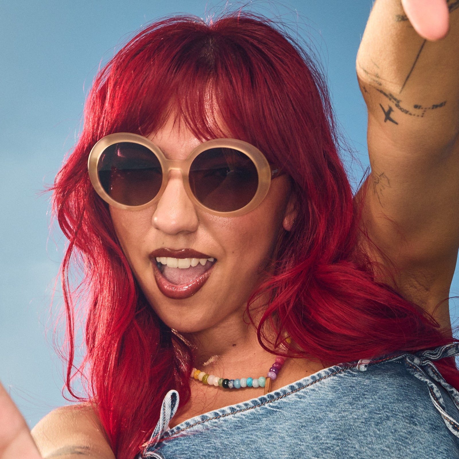 Woman poses wearing oversized round beige sunglasses with purple gradient lenses.