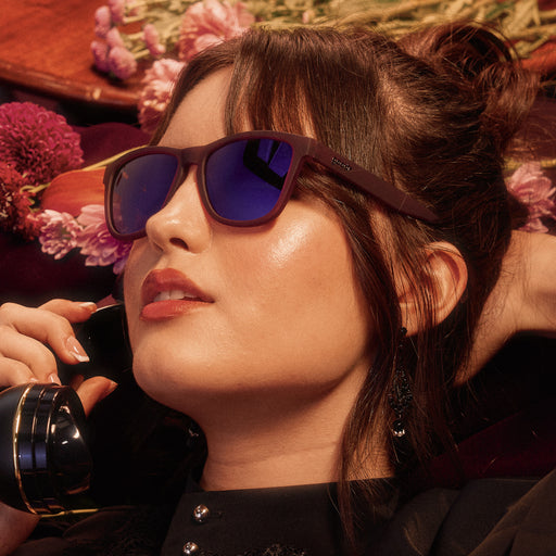 Side profile of a woman on the phone wearing translucent purple sunglasses with reflective purple lenses.