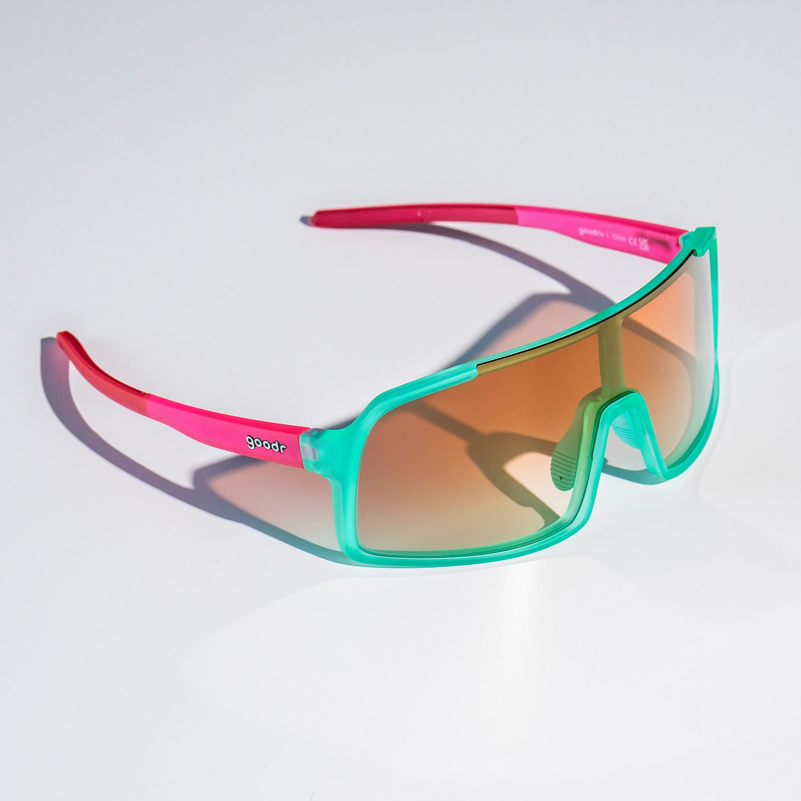 Three-quarter view of teal wrap sunglasses with amber gradient lenses sitting on a white surface.
