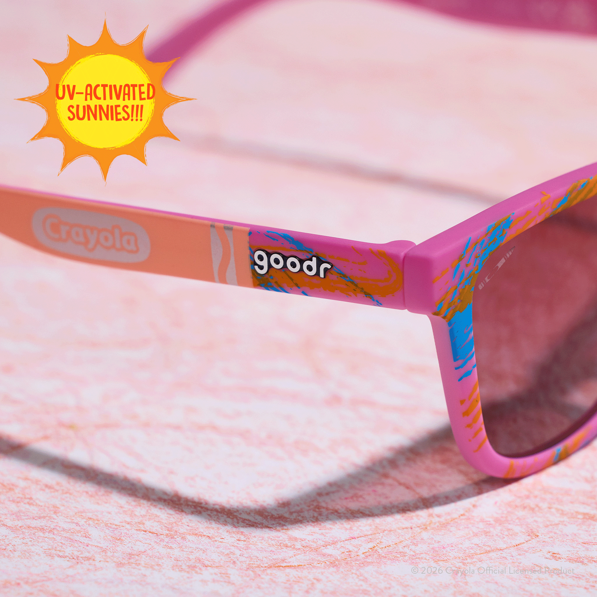 Close-up of Crayola goodr UV-activated Summertime sunglasses with tan-to-magenta frames and rose ocean gradient lenses.