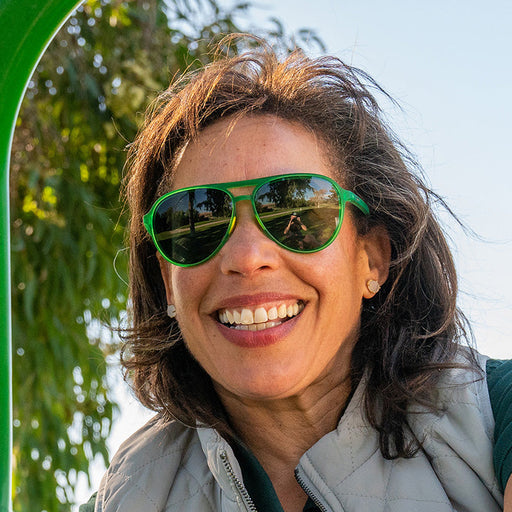 A woman wearing green aviator sunglasses with non-reflective lenses smiles into the camera.