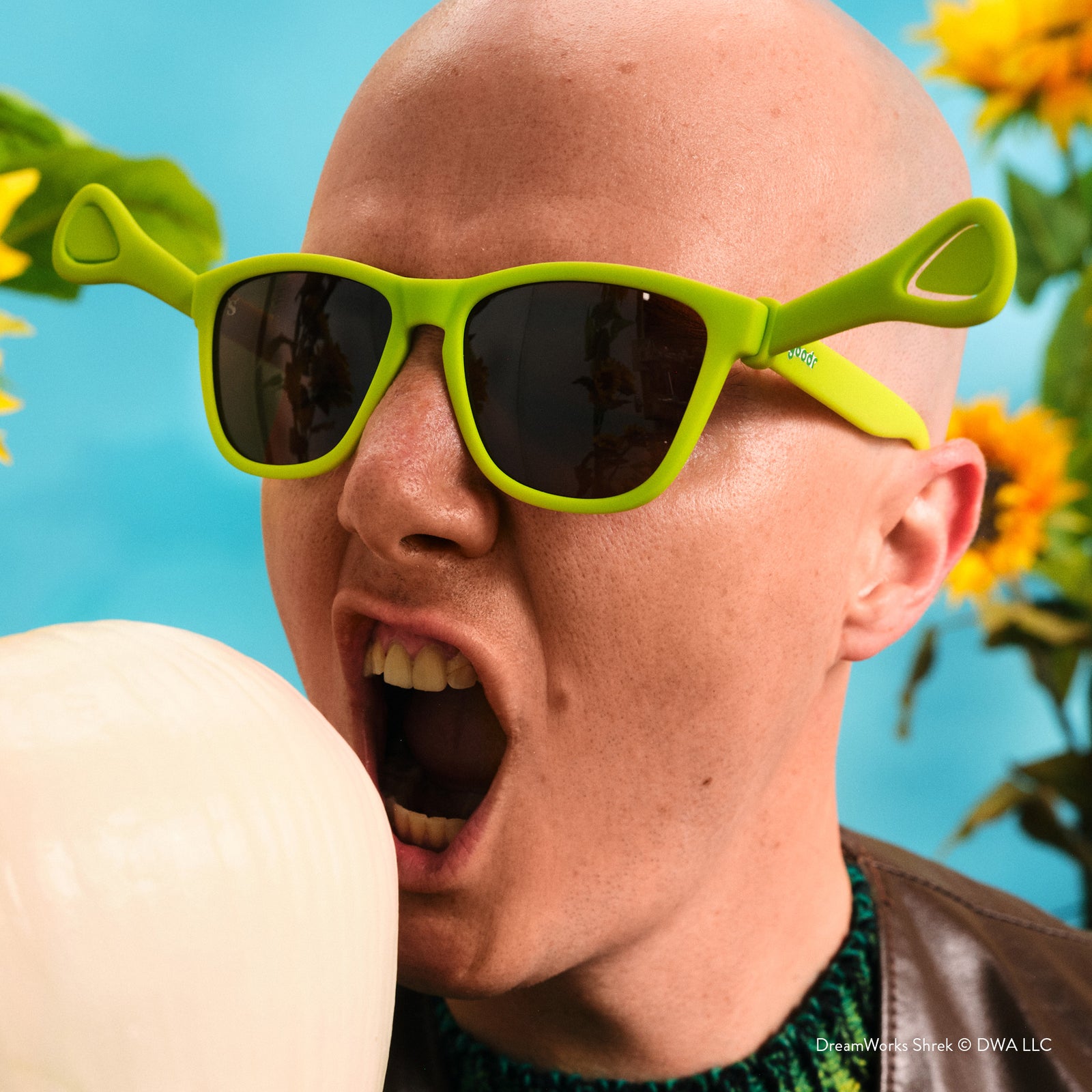 Person wearing bright green sunglasses with a blue background and sunflowers.