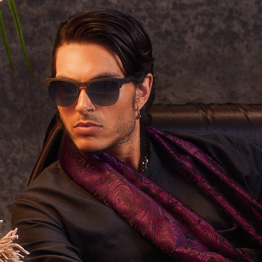 A man elegantly posing while wearing gray translucent half-rim frames featuring gradient gray lenses.